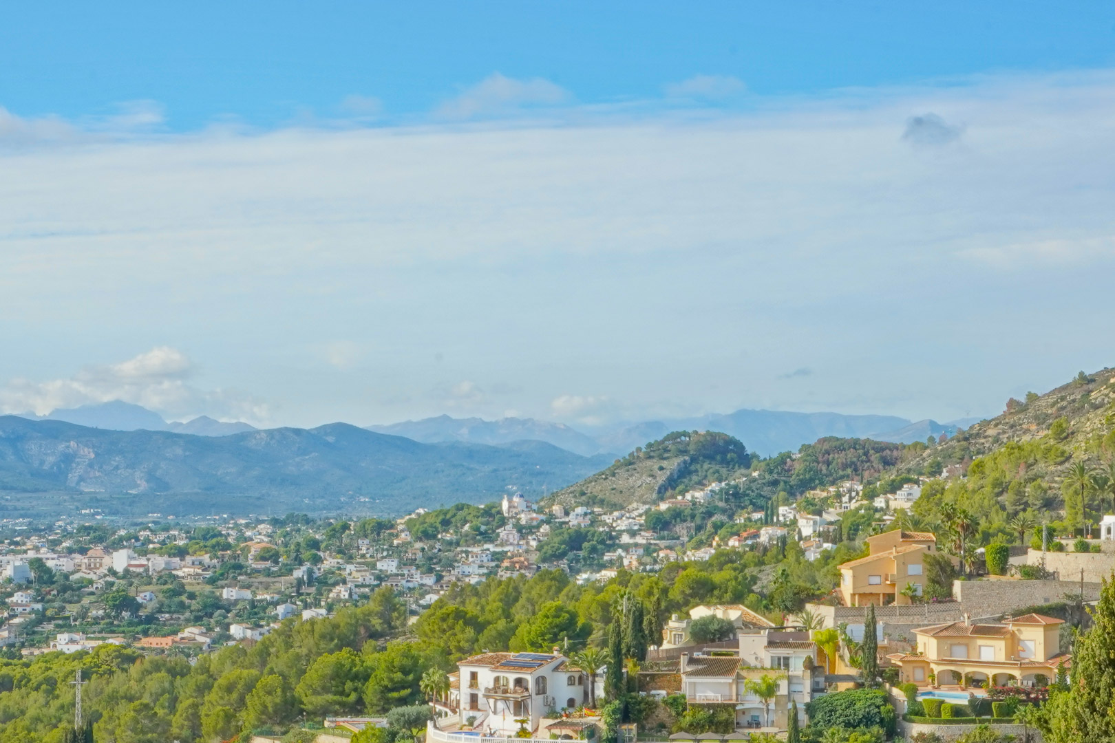 Panoramic view from the property overlooking the valley and surrounding mountain ranges, showcasing Mediterranean greenery and the residential landscape.
