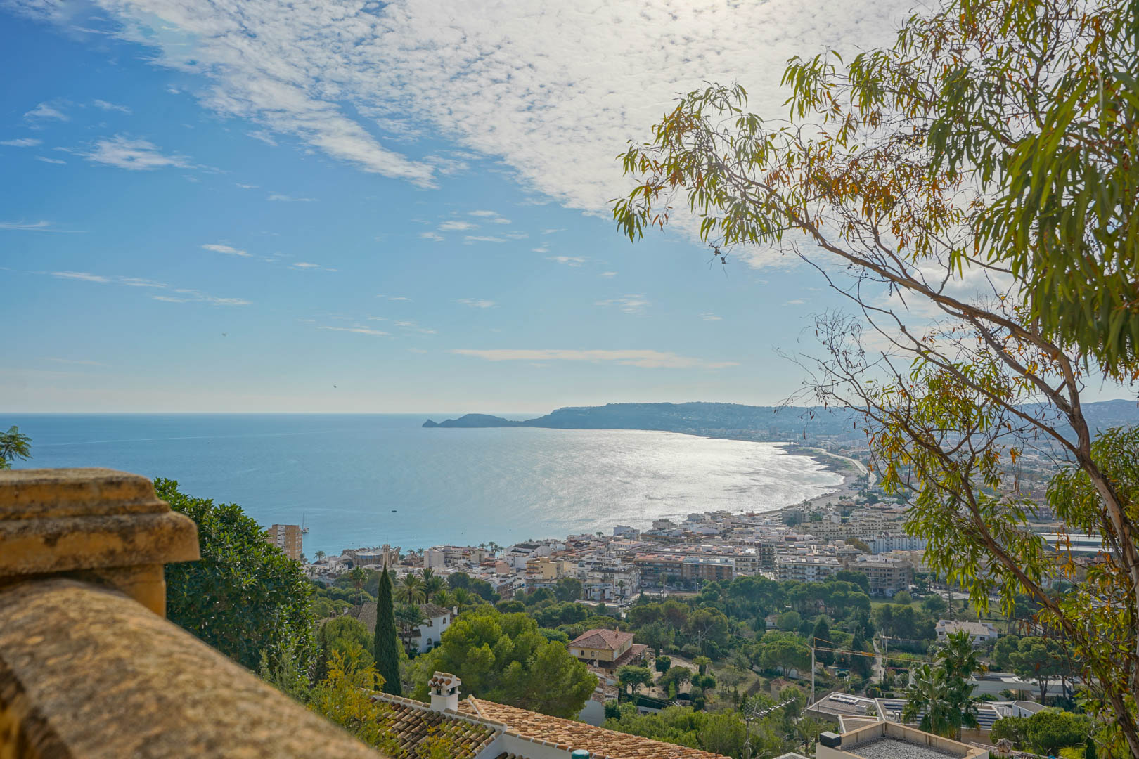 Panoramic view from the terrace overlooking Jávea Bay and Cap Negre, featuring the coastal town and Mediterranean Sea under a bright sky.