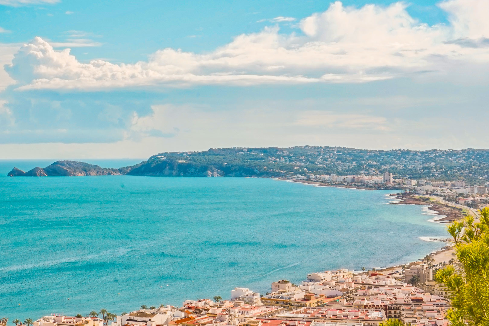 Panoramic view of Jávea Bay from La Corona, showcasing the coastal town architecture and the Cap Negre headland against the turquoise Mediterranean Sea.