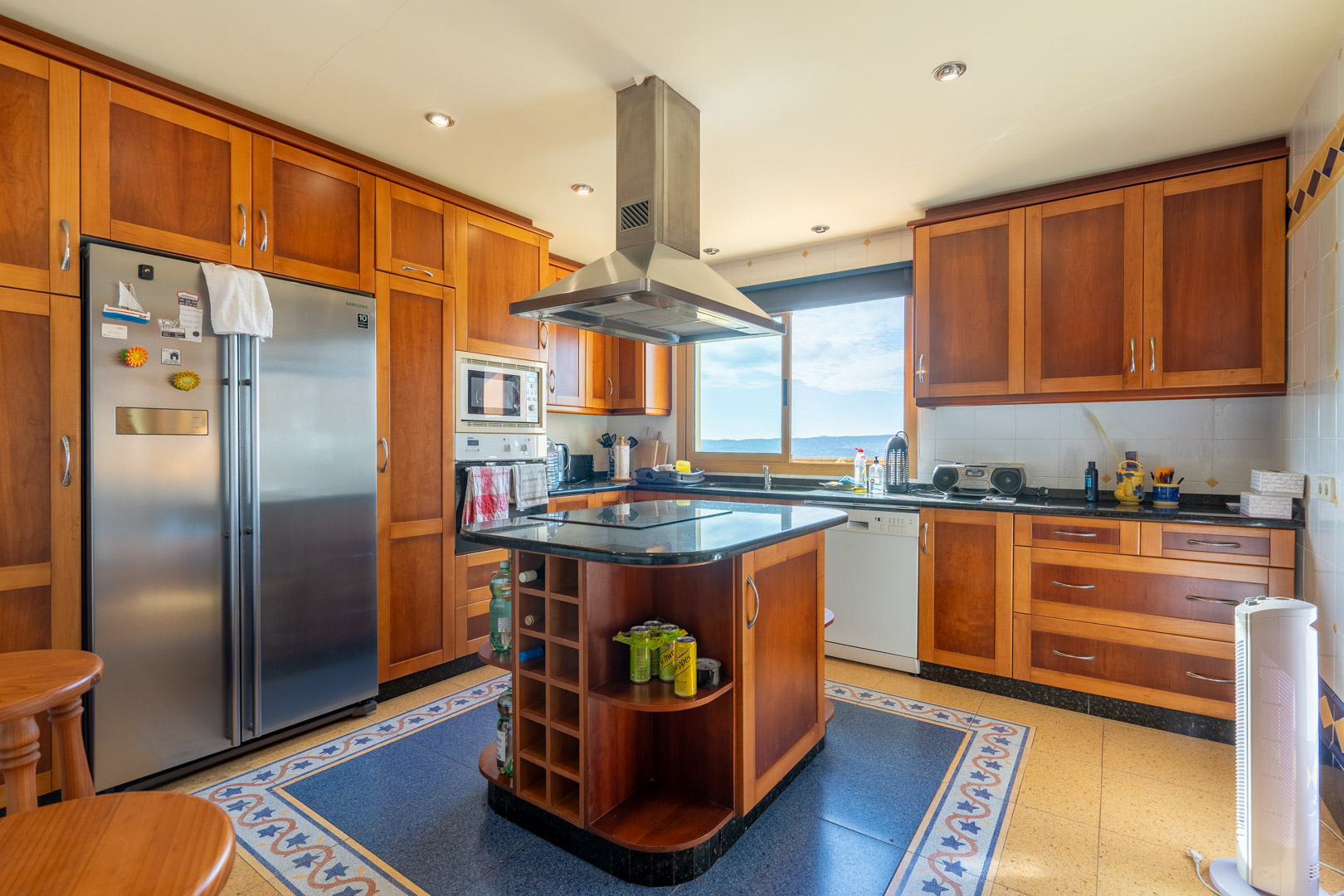Traditional kitchen featuring wooden cabinetry, a central island with black granite countertop, and a stainless steel extractor. Includes integrated appliances and sea views.