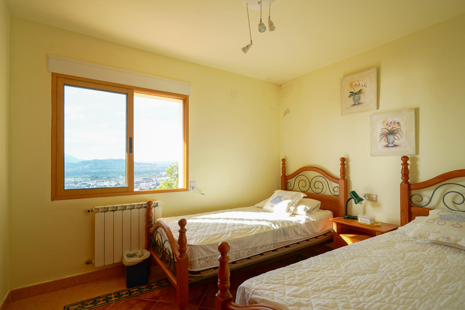 Twin bedroom featuring wooden bed frames with iron details, tiled flooring, and a large window overlooking the scenic valley and mountain landscape.
