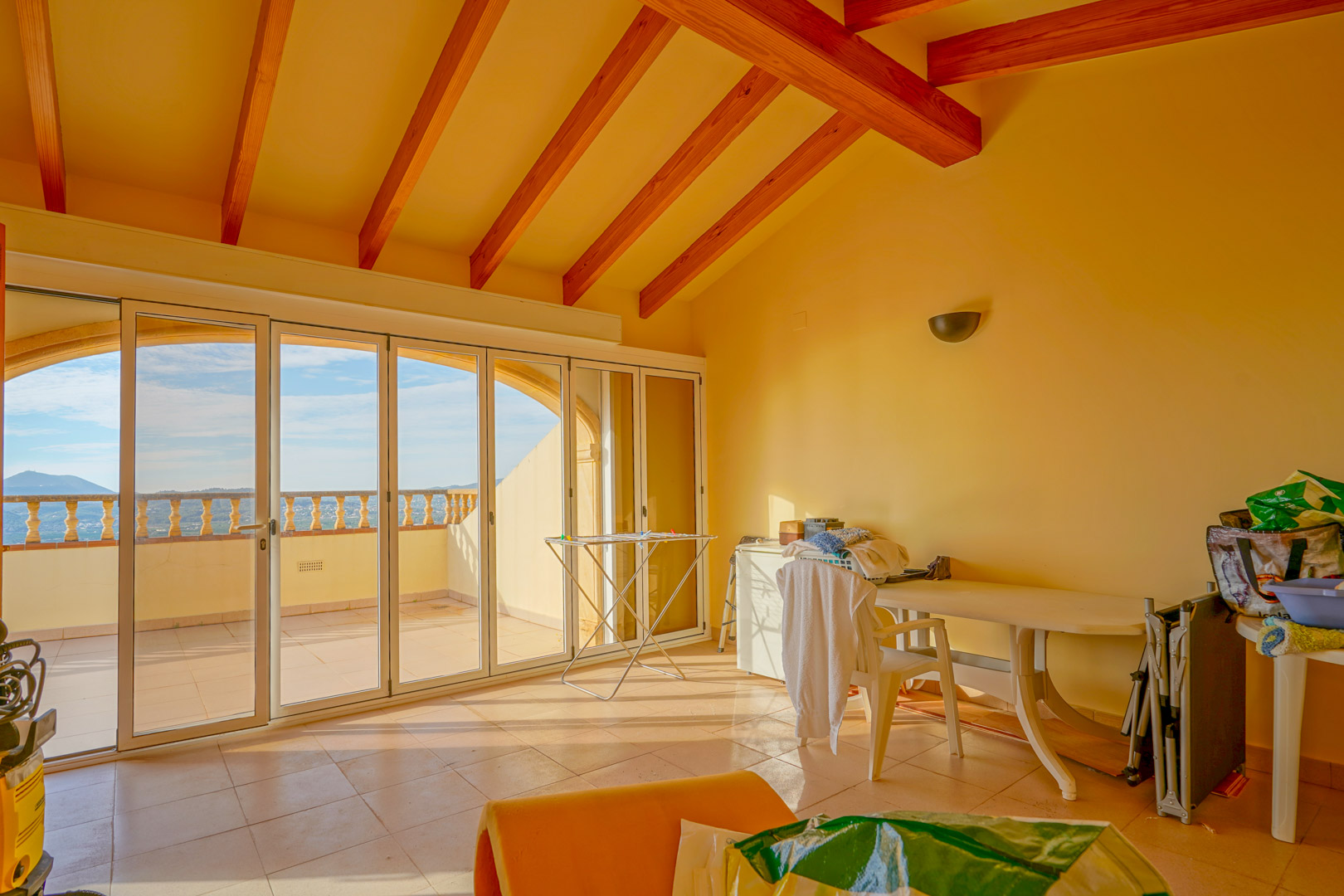 Upper-floor room featuring high ceilings with exposed wooden beams and large glass doors opening onto a terrace with panoramic mountain views.