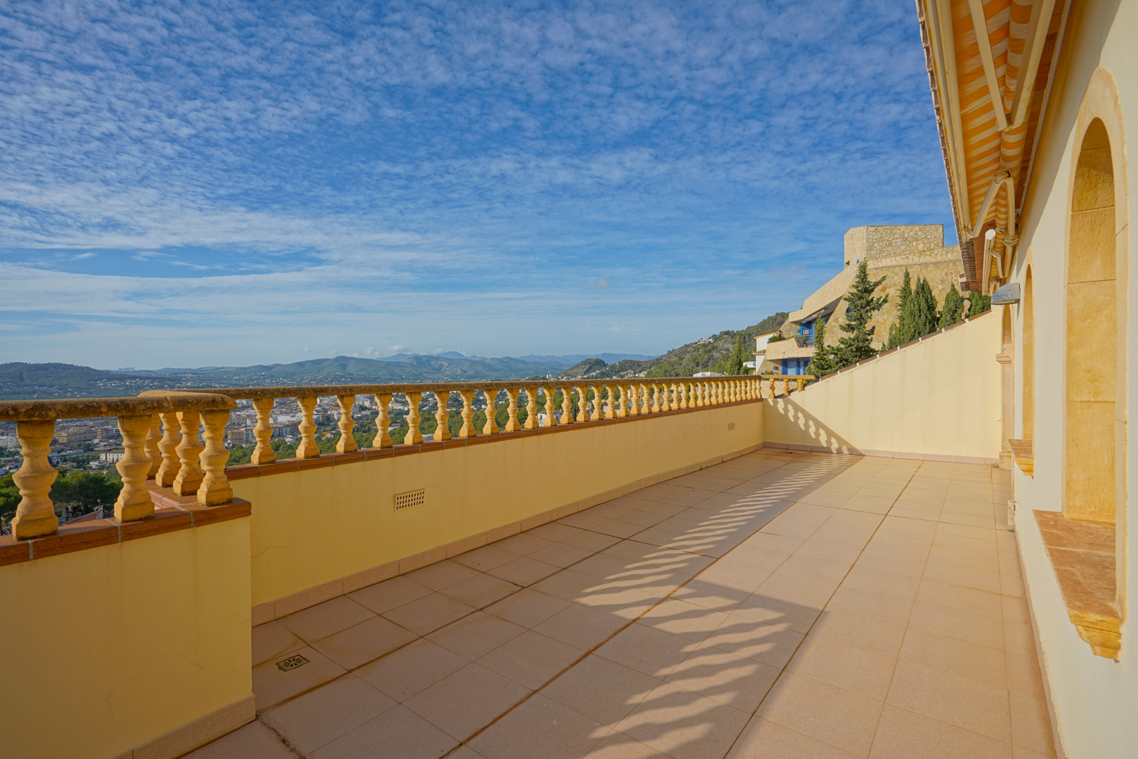 Upper terrace featuring a traditional stone balustrade and tiled flooring, providing expansive views of the Jávea valley and distant mountain ranges.