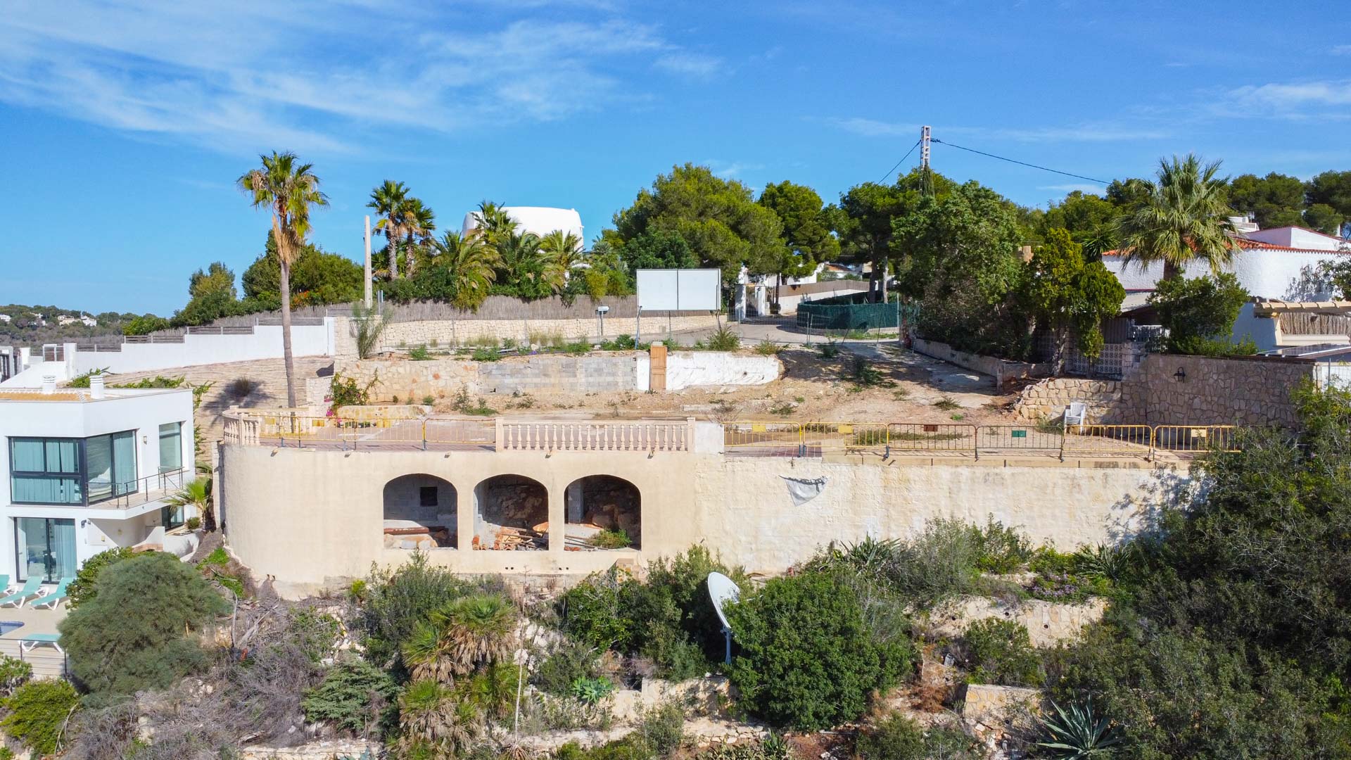 Elevated building plot featuring an existing arched sub-structure, stone retaining walls, and native Mediterranean flora, prepared for a luxury villa project.