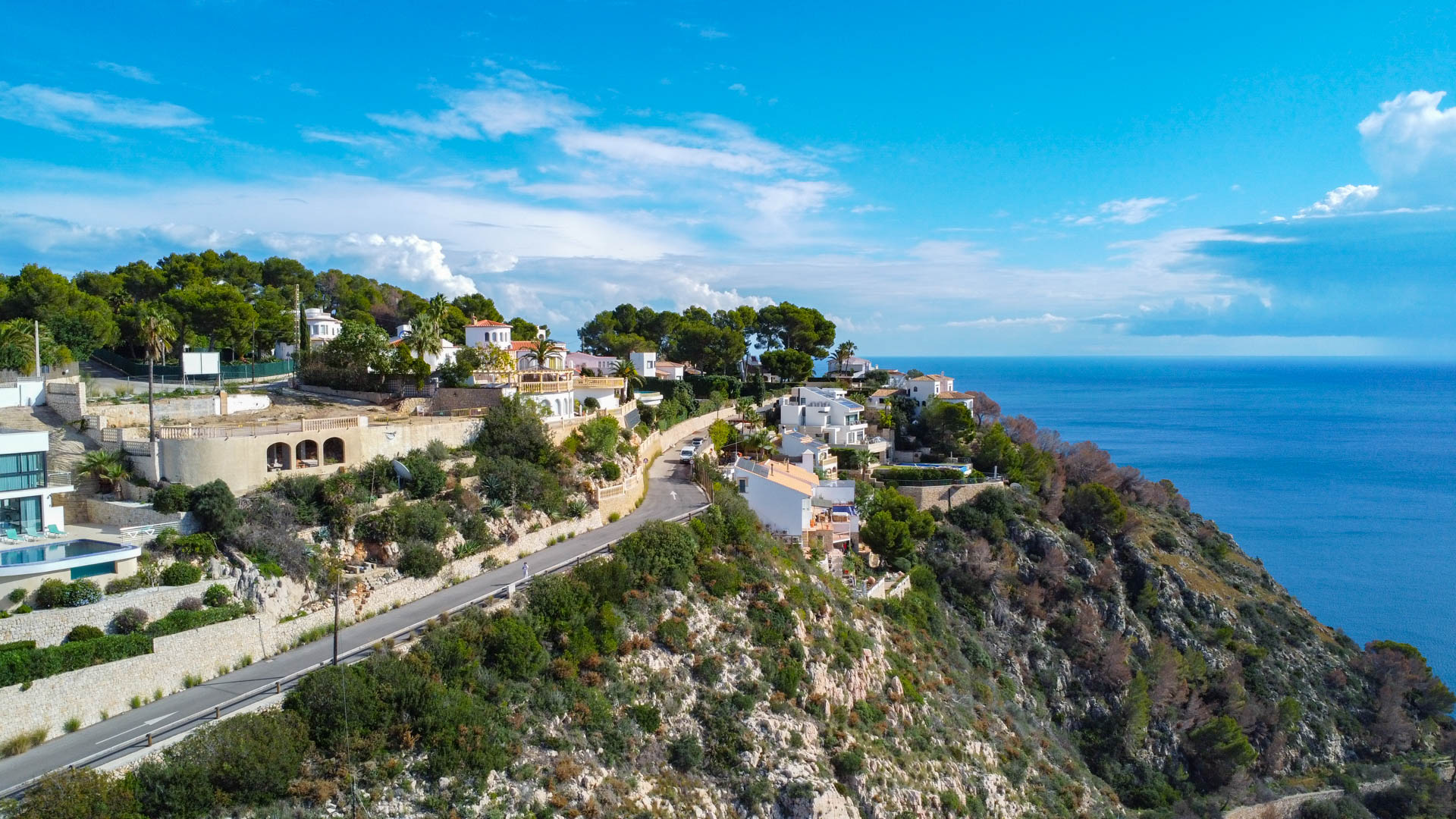 Elevated view of the cliffside plot in Granadella, featuring paved road access and panoramic vistas of the Mediterranean Sea and rugged coastline.