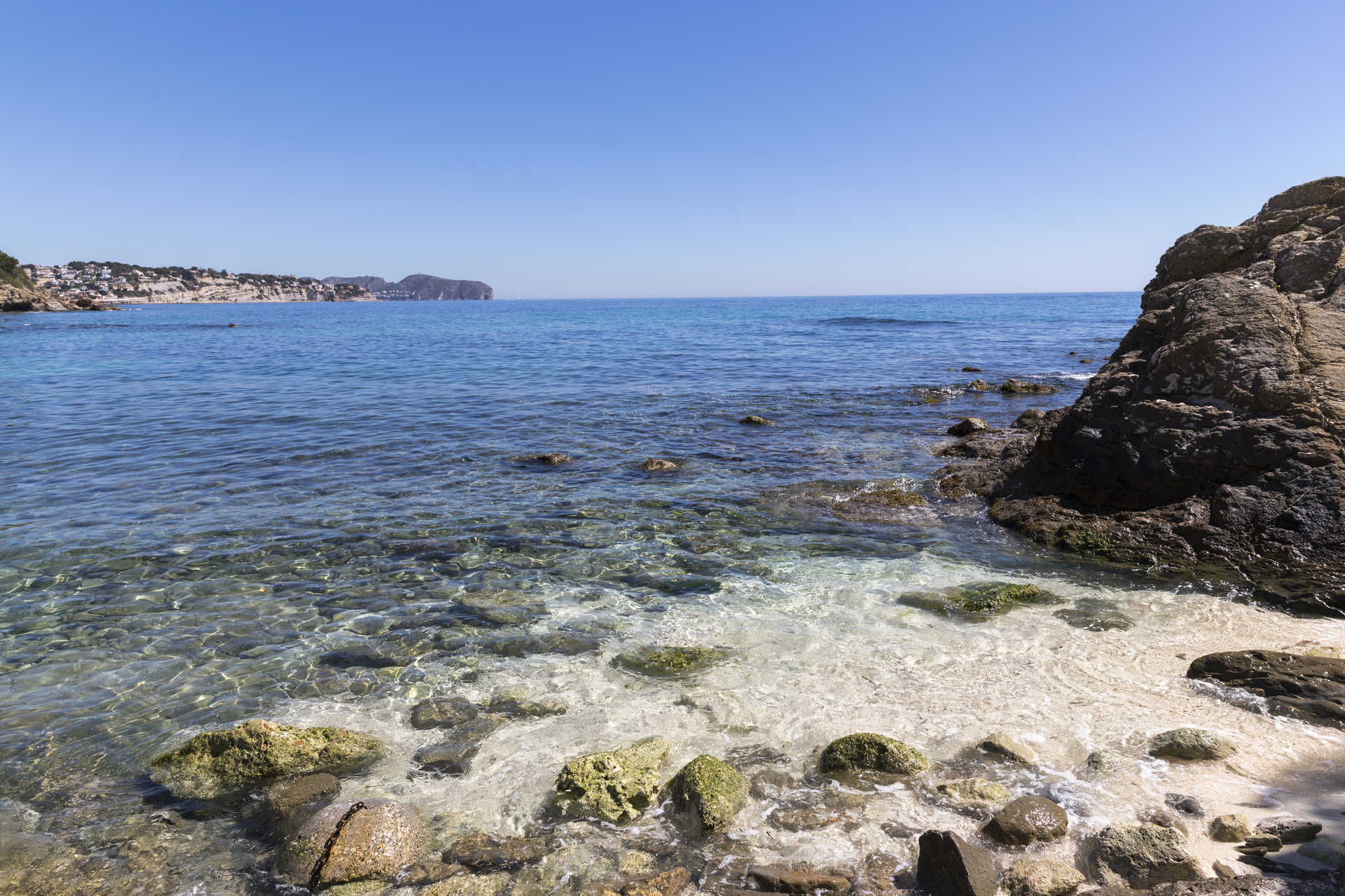 View of the Mediterranean coastline featuring crystal-clear waters and a rocky shoreline near La Fustera beach, illustrating the villa's coastal surroundings.