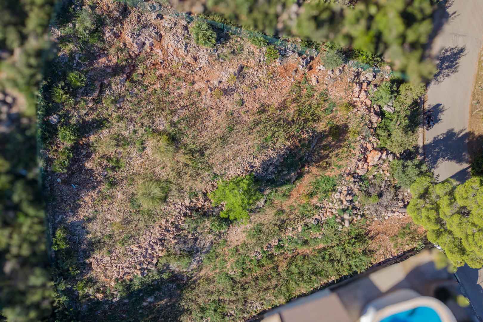 Overhead aerial view of the fenced plot in Montepego, featuring natural rocky terrain and direct access from the paved residential road.
