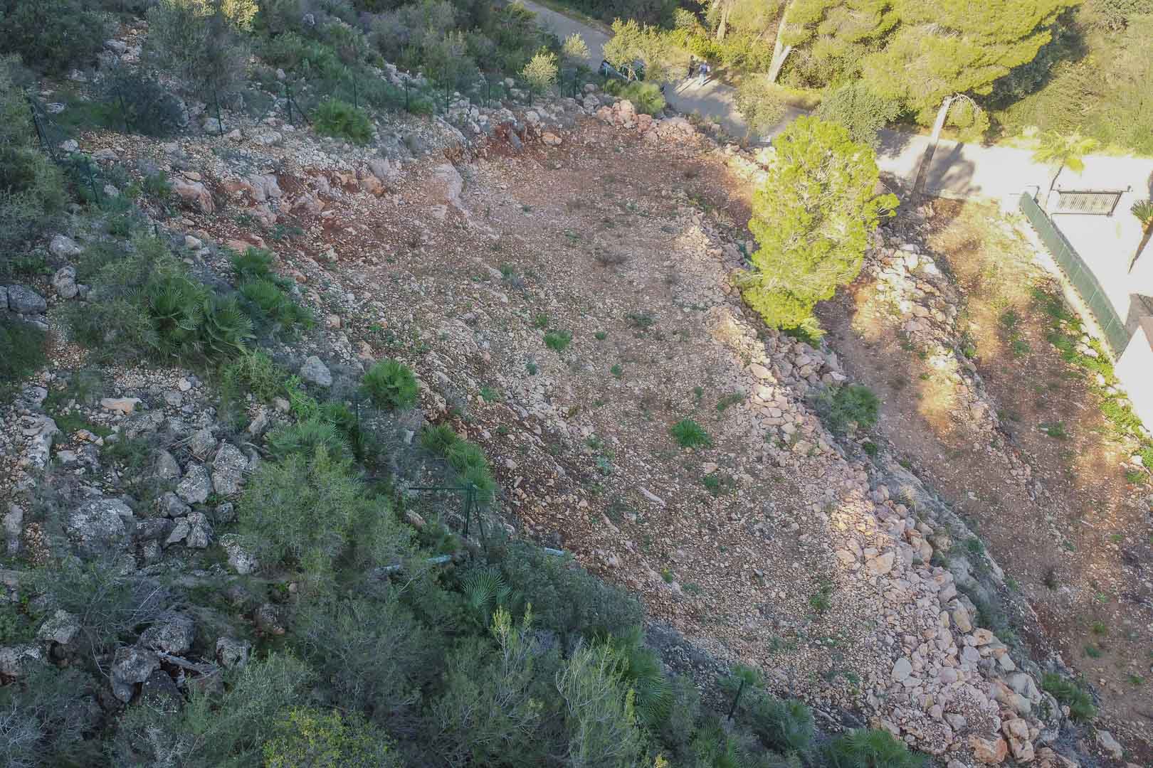 Terraced building plot in Montepego featuring cleared rocky terrain, perimeter fencing, and surrounding Mediterranean flora with direct road access.