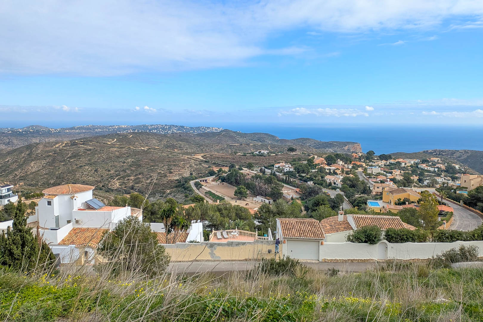 Elevated panoramic views from Cumbre del Sol towards the Mediterranean Sea, showcasing the coastal residential landscape and surrounding natural hills.