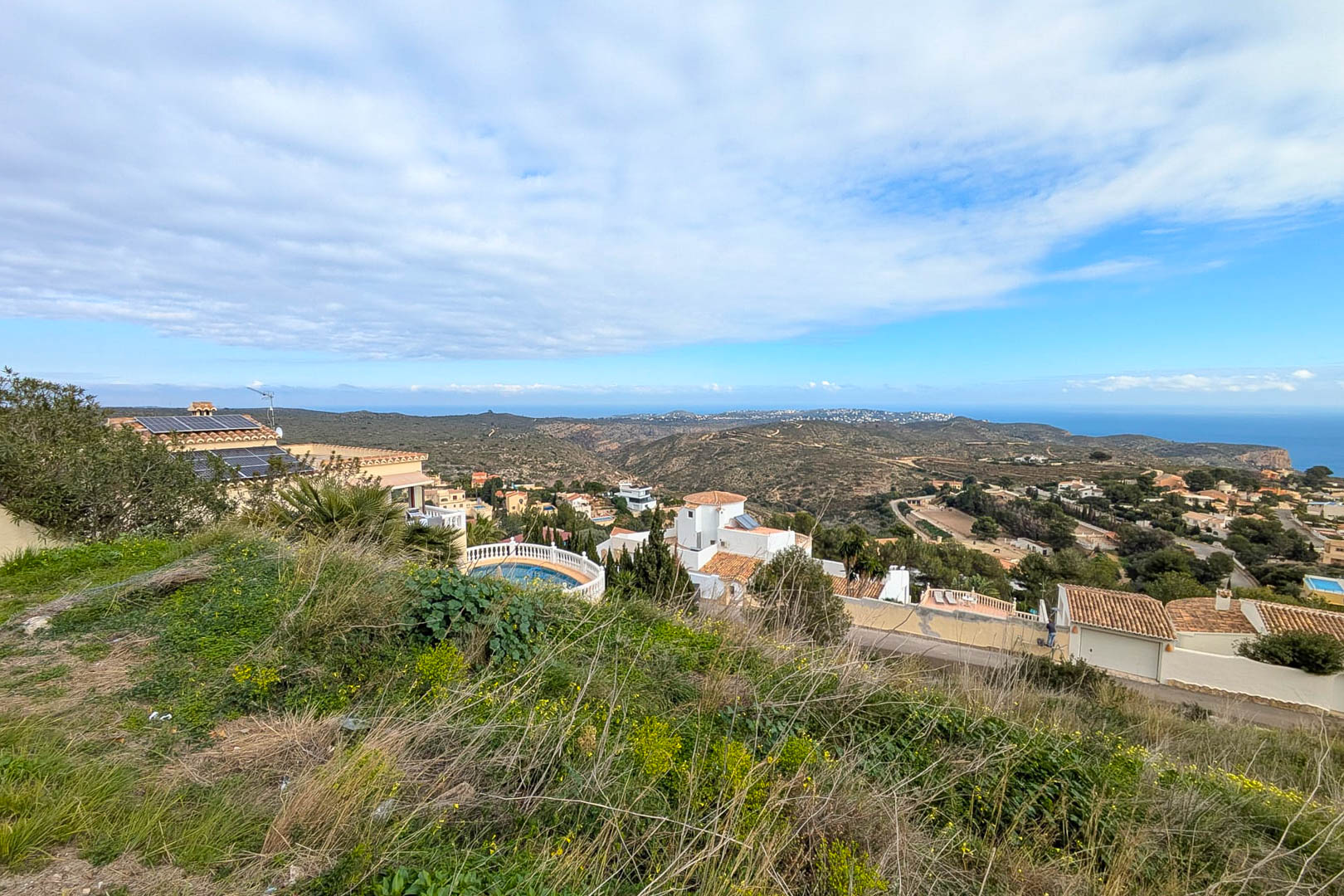 Panoramic views from the elevated plot overlooking the Mediterranean Sea and valley, featuring natural hillside vegetation and surrounding residential villas.