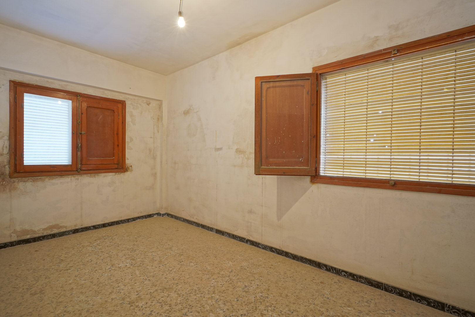 Bedroom for renovation featuring original terrazzo flooring, wooden window frames with shutters, and walls ready for a fresh update.