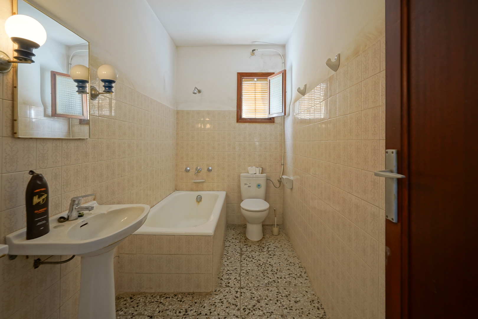 Functional bathroom featuring a built-in bathtub, pedestal sink, terrazzo flooring, and classic patterned wall tiles with a small window.