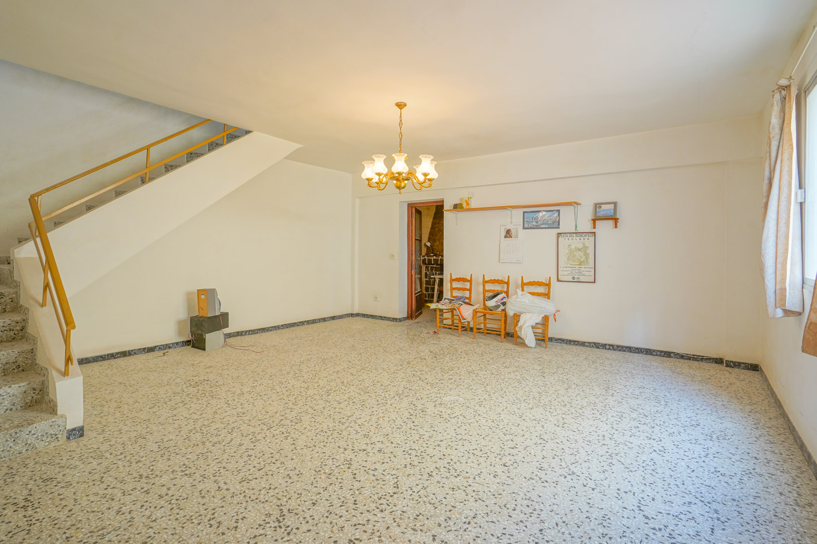 Main living area featuring original terrazzo flooring, a classic chandelier, and a staircase with a metal handrail leading to the upper floor.