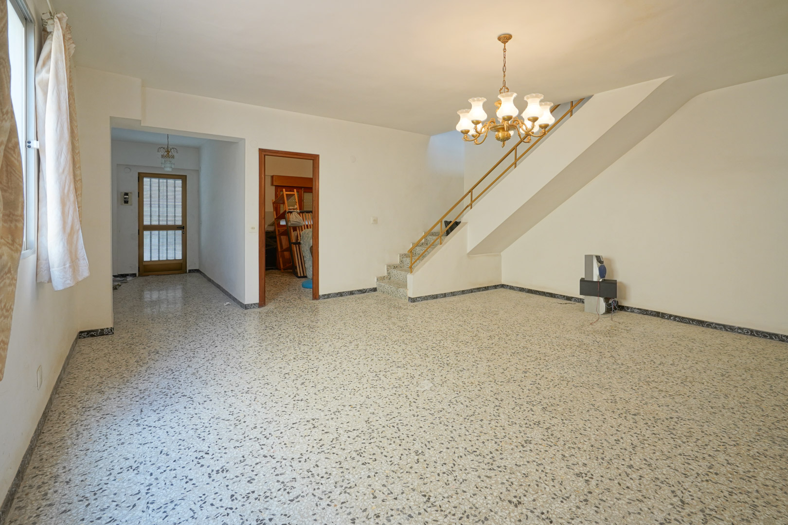 Main living room featuring original terrazzo flooring, a built-in staircase with metal railings, and access to the entrance hall.