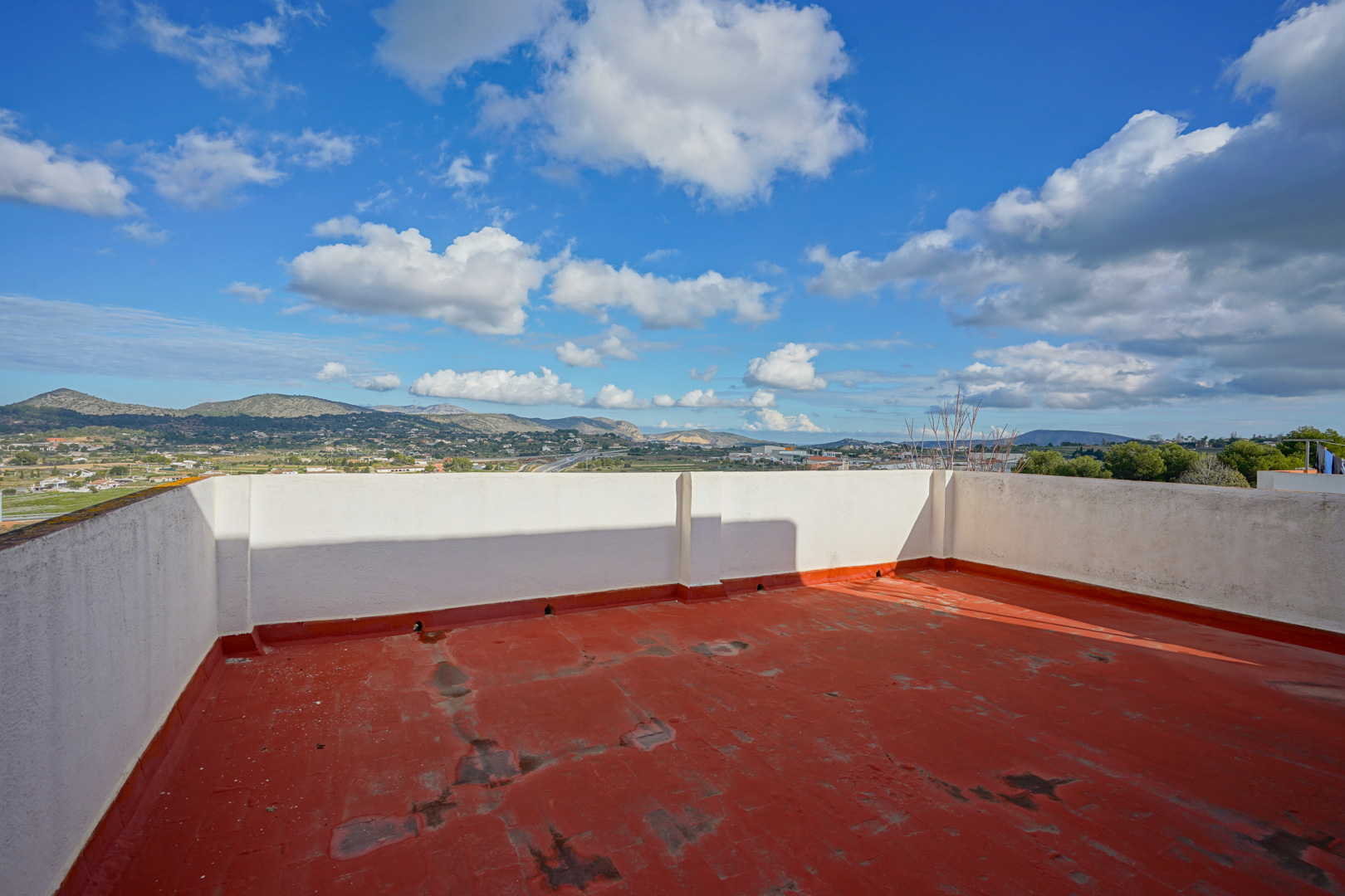 Rooftop terrace featuring red-toned flooring and white perimeter walls, providing panoramic views of the surrounding mountains and inland landscape.