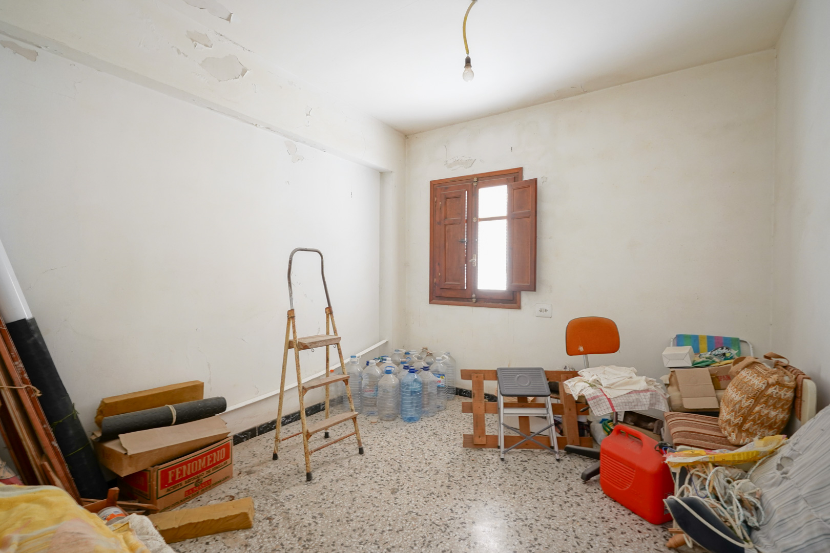 Room featuring original terrazzo flooring and a wooden window with shutters. The space illustrates the renovation potential and the authentic character of the property.