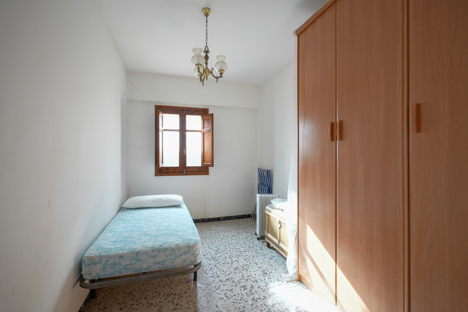 Single bedroom featuring traditional terrazzo flooring, a large wooden wardrobe, and a natural wood window with integrated shutters.
