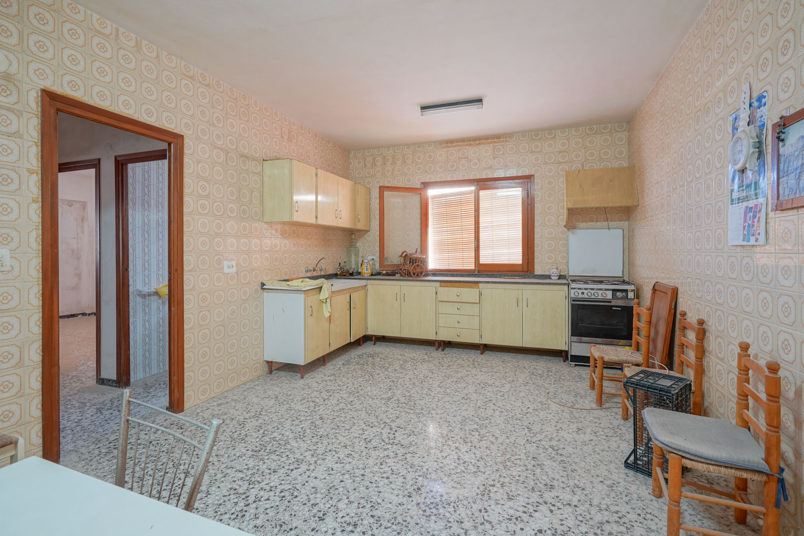 Spacious kitchen featuring vintage patterned wall tiles, terrazzo flooring, and light wood cabinetry with natural light from a central window.