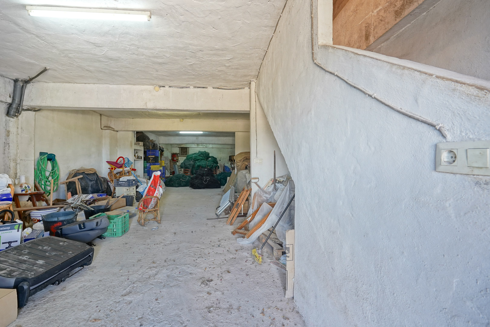 Spacious semi-basement garage featuring concrete flooring and plastered walls. It includes a side staircase providing direct access to the main living areas.