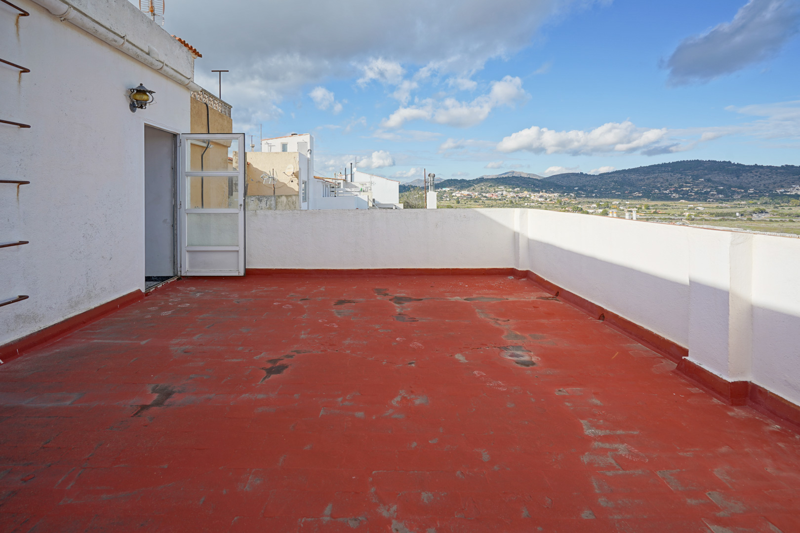 Upper terrace featuring red tiled flooring and white perimeter walls, providing panoramic views of the surrounding mountains and countryside.