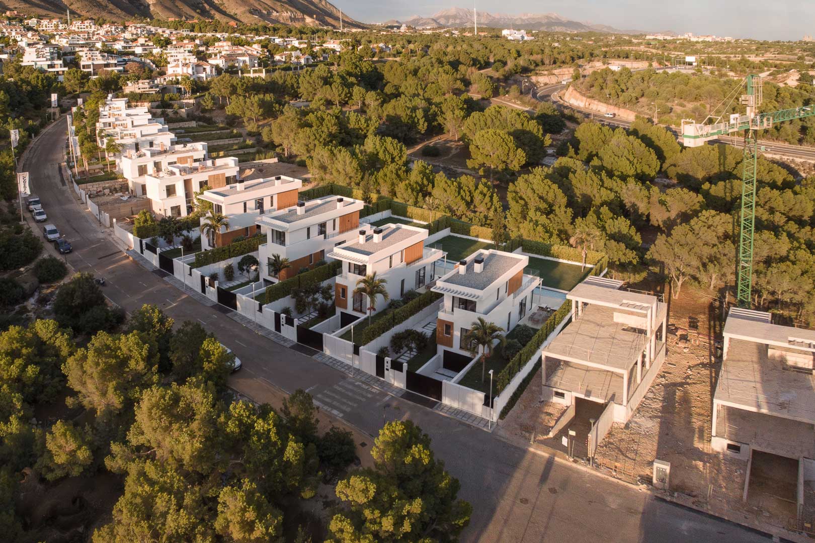 Aerial view of the residential complex featuring modern white villas with wood accents, private pools, and landscaped gardens, nestled between pine forests and mountains.