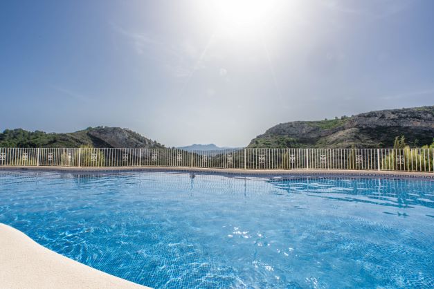 Communal swimming pool at Monte Cala Gardens featuring blue tiling and panoramic views of the surrounding mountains and nature park.