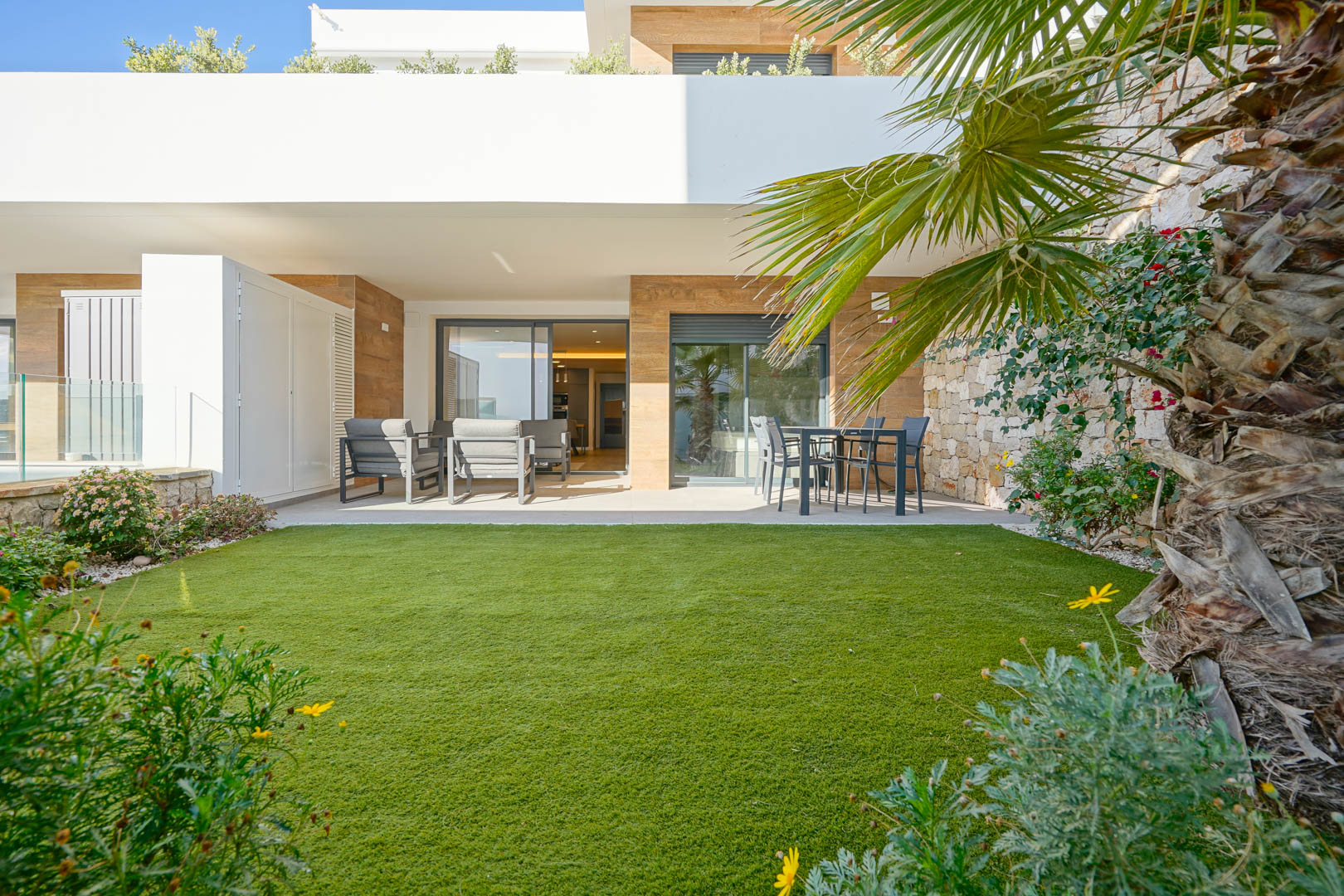 Covered 23 m2 terrace with lounge and dining areas, leading to a 36 m2 private garden with artificial turf and a characteristic natural stone wall.