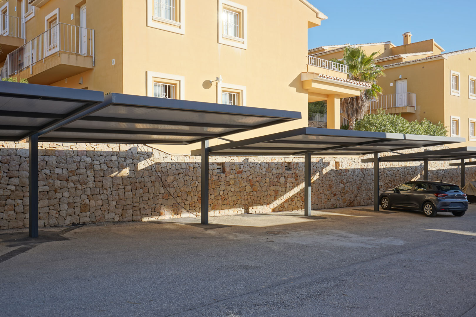 Covered parking area featuring modern metal carports and a natural stone retaining wall, located directly in front of the residence.
