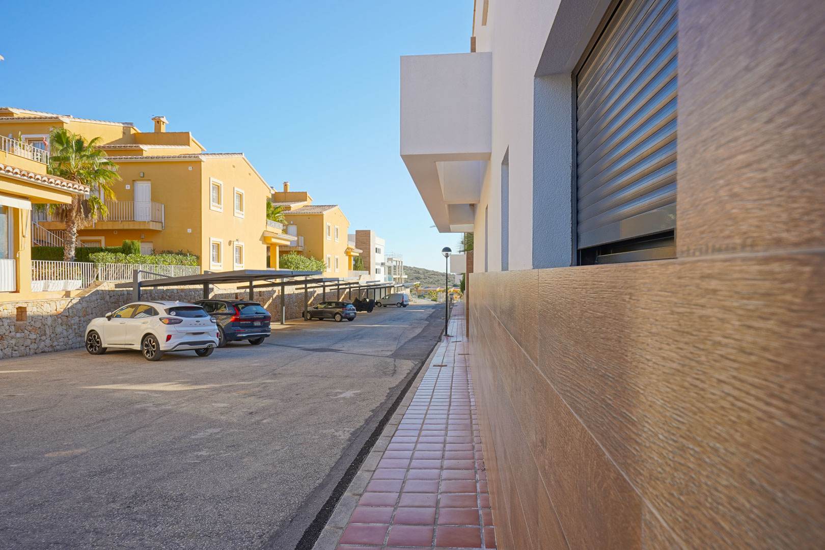 Covered parking area situated in front of the modern facade, featuring wood-effect tiling and integrated electric shutters.