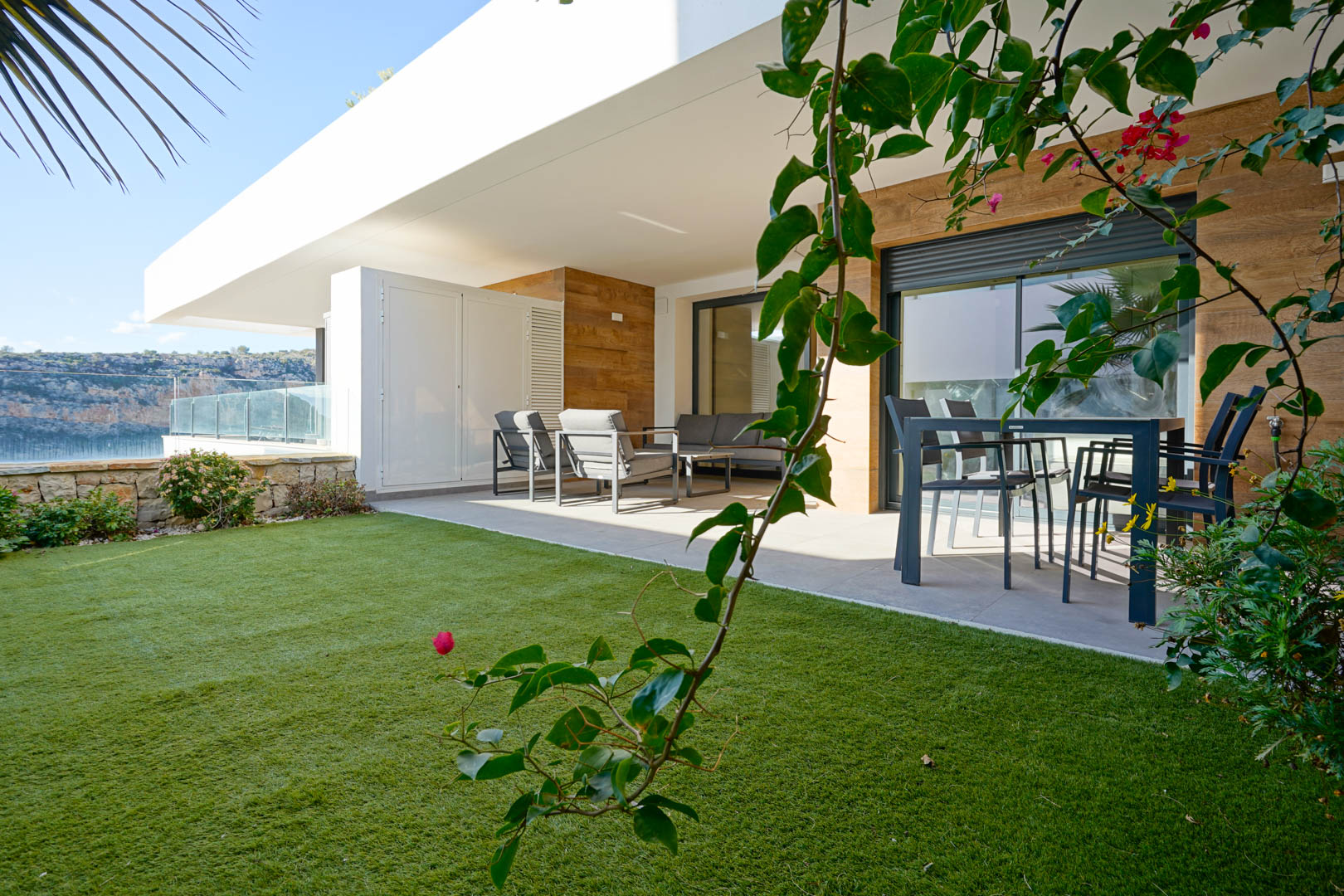 Covered terrace featuring modern outdoor lounge and dining sets, adjacent to a private lawn with natural stone walls and views of the nature reserve.