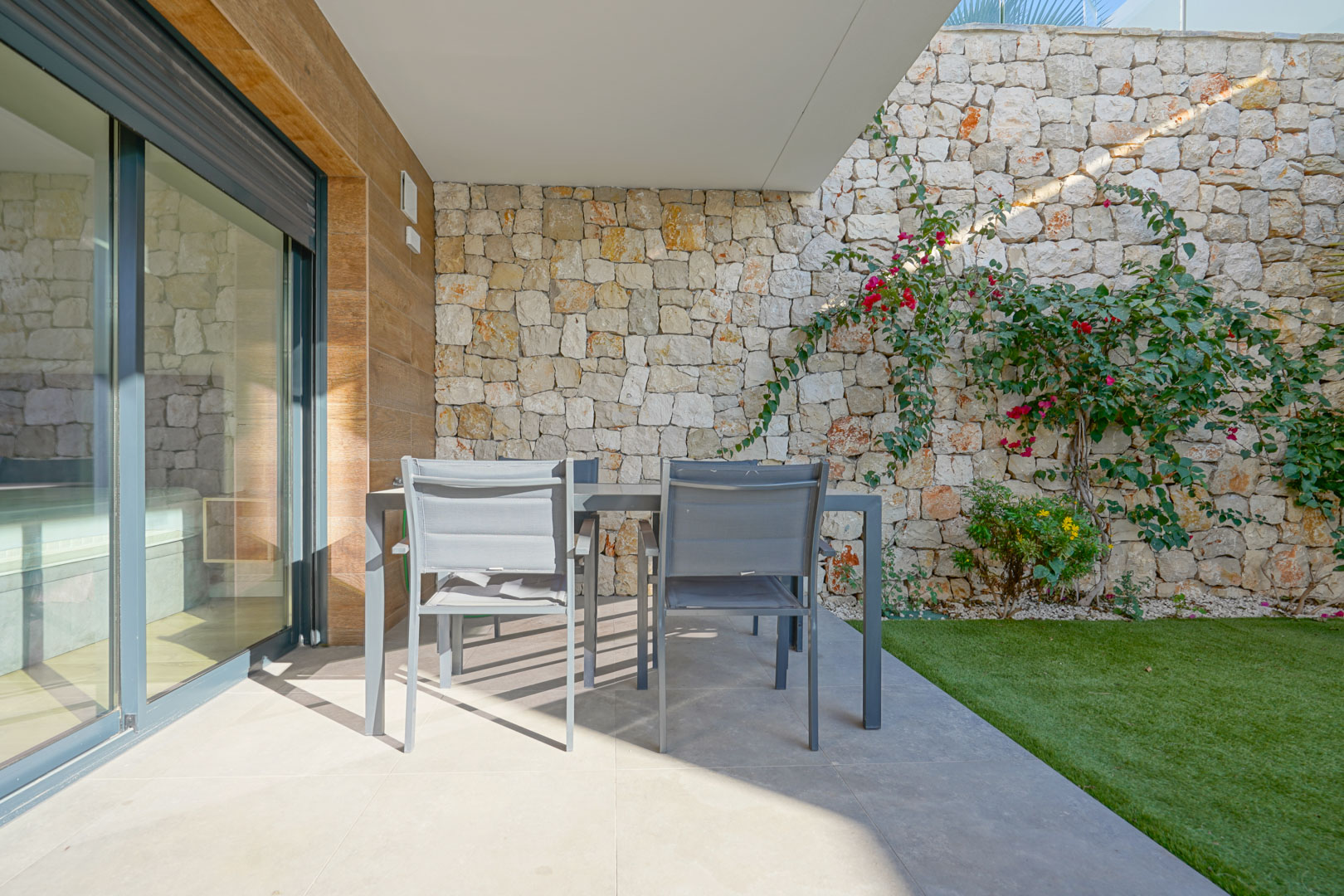 Covered terrace with outdoor dining area, featuring natural stone walls and a private garden with artificial grass.