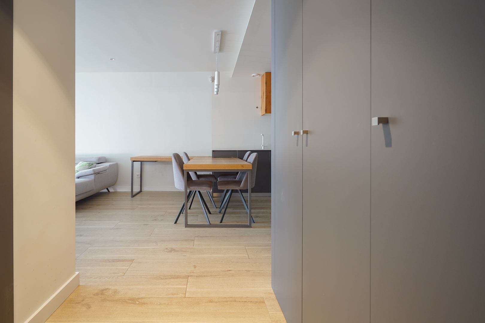 Entrance view featuring grey built-in storage, light wood flooring, and an open-plan dining area with a wooden table and modern pendant lighting.
