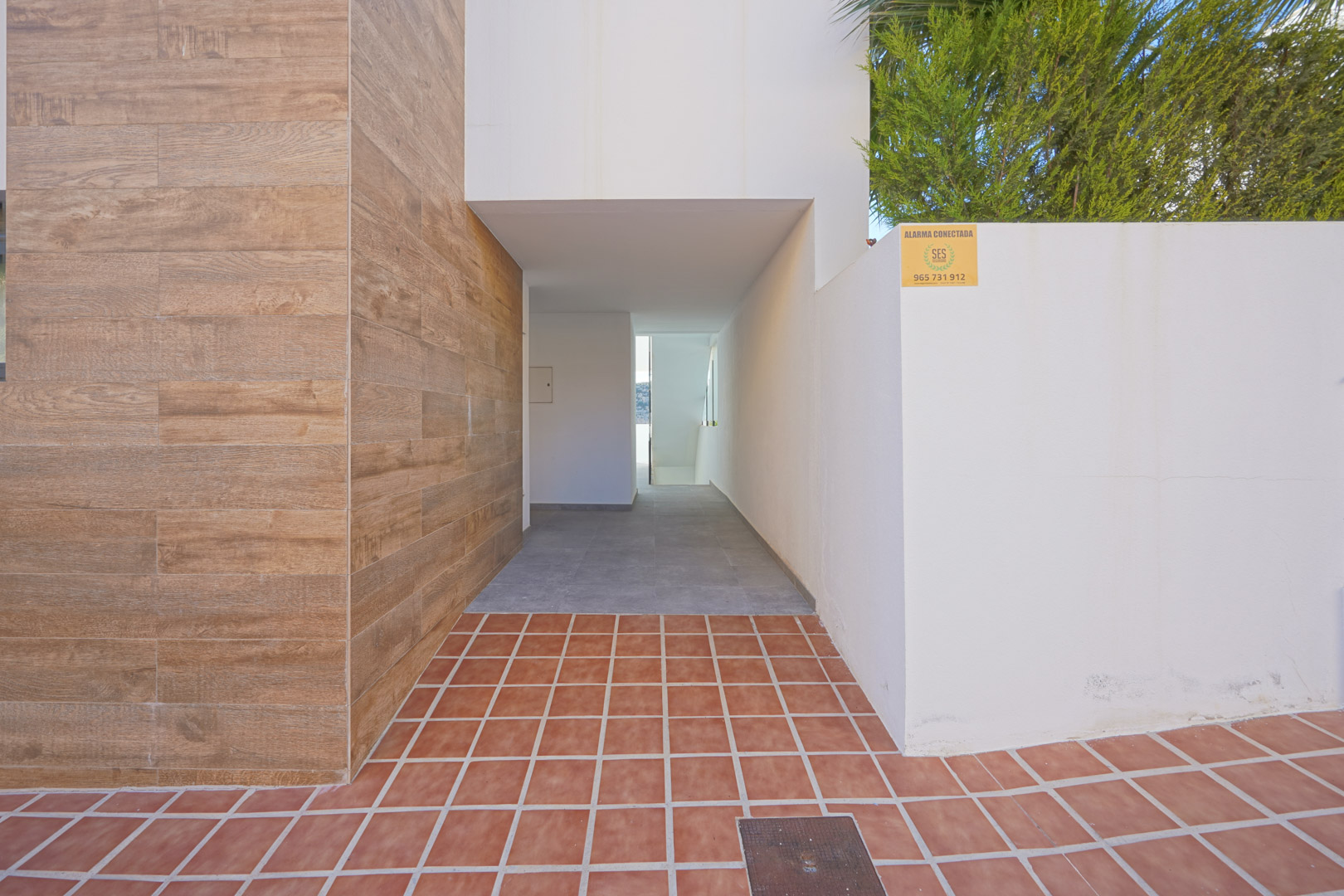Exterior entrance featuring wood-effect wall cladding, terracotta tiling, and a covered walkway leading to the apartment's access points.