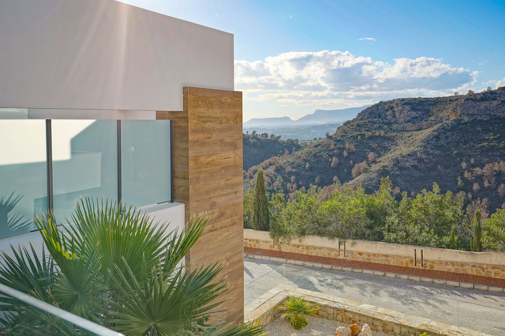 Exterior view from the terrace featuring glass railings, modern wood-effect cladding, and panoramic views over the surrounding natural park and mountains.