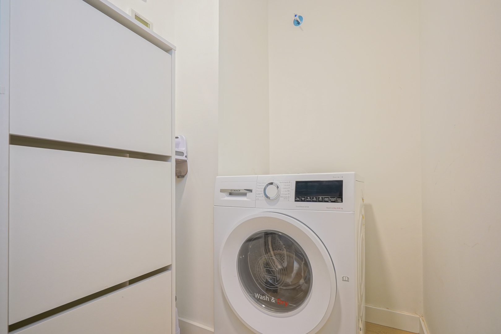Functional utility room featuring a Bosch washer-dryer and integrated white storage cabinetry, conveniently located off the entrance hall.
