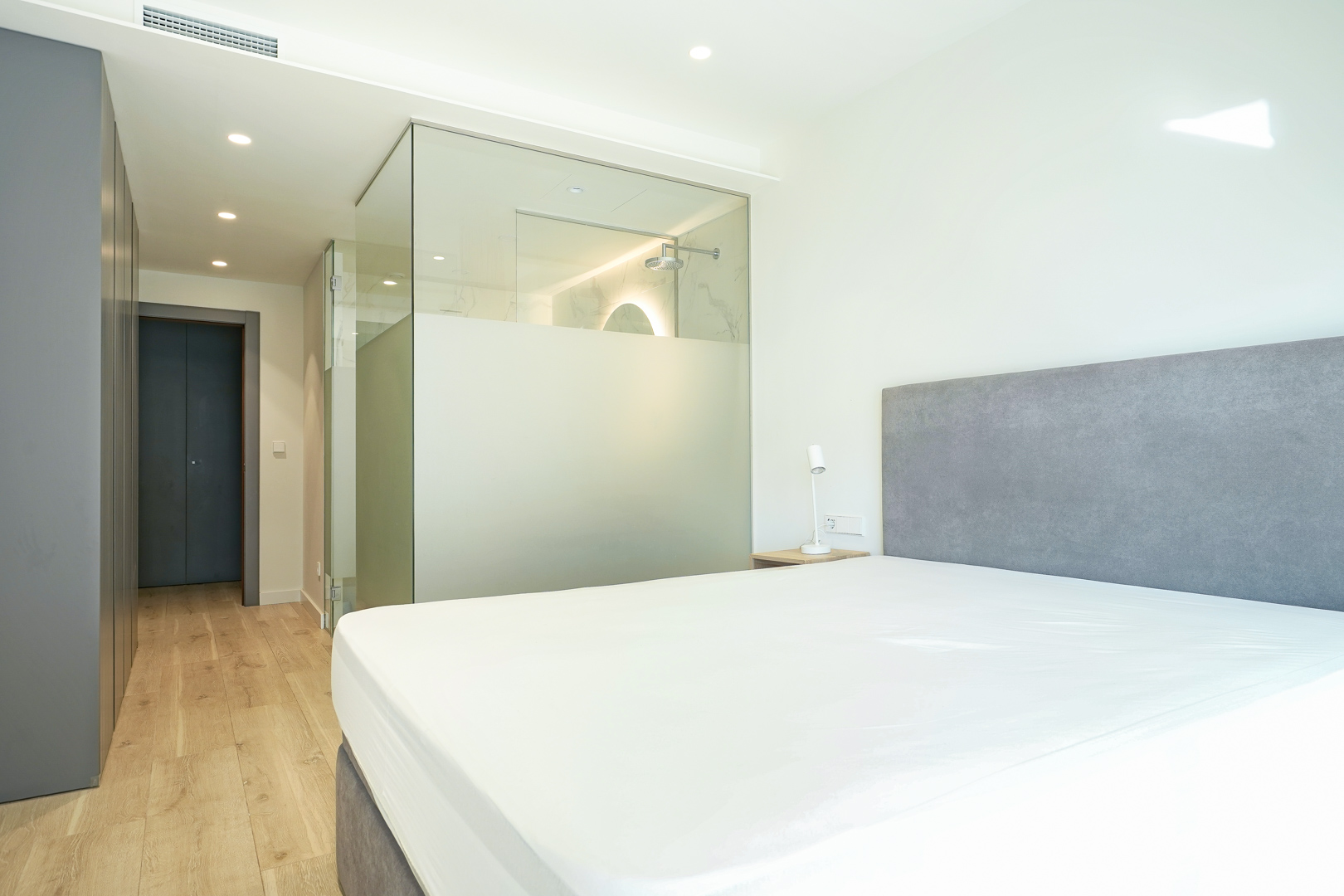 Master bedroom featuring an integrated en-suite bathroom with glass partitions, built-in wardrobes, and light wood flooring.