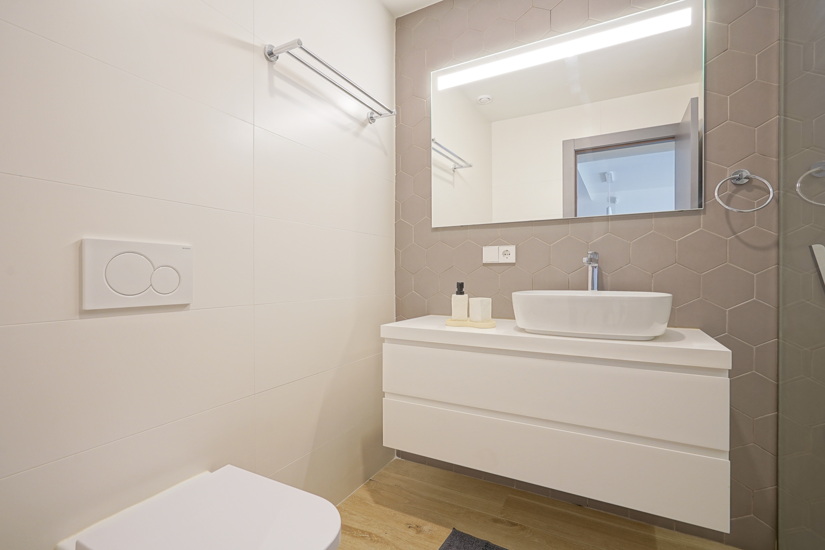 Modern bathroom featuring a taupe hexagonal tile backsplash, a white floating vanity with a vessel sink, and a large mirror with integrated LED lighting.