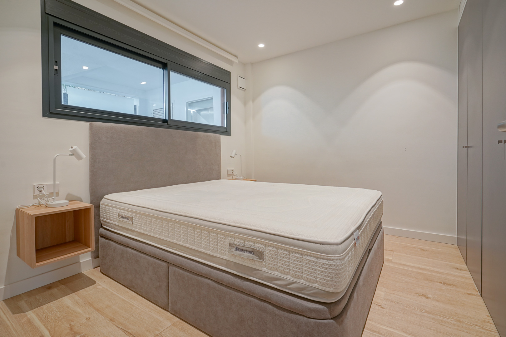 Modern bedroom featuring a double bed with upholstered headboard, built-in wardrobes, and light wood flooring with recessed lighting.