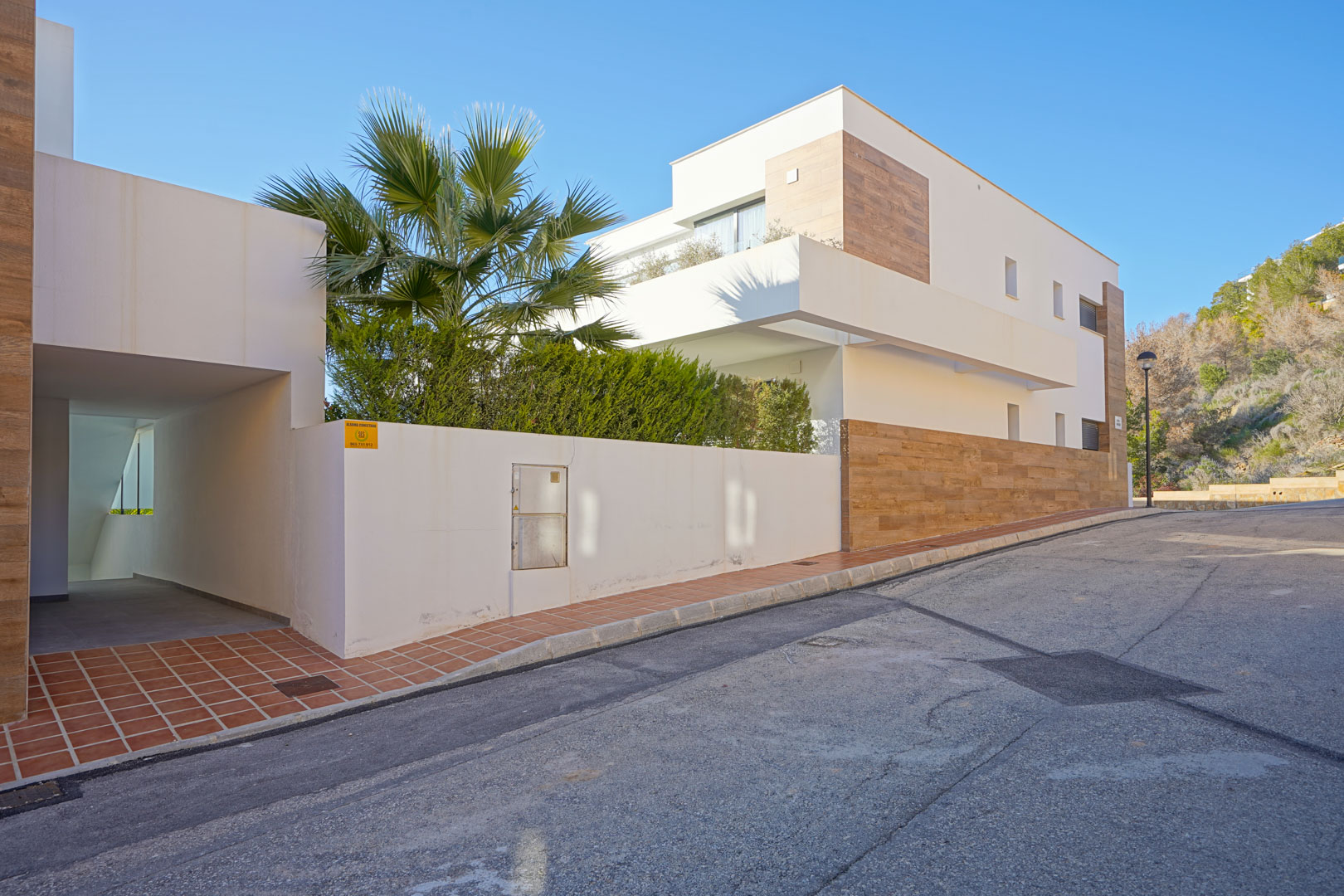 Modern exterior of the Monte Cala Gardens residence featuring white facades with wood-effect accents and a covered pedestrian entrance under a clear sky.
