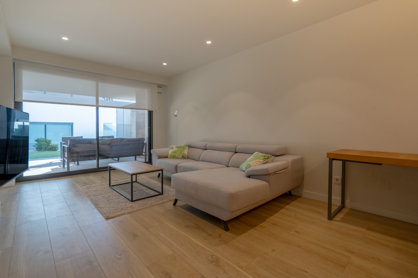 Modern living room featuring a grey chaise longue sofa, light wood flooring, and large sliding doors opening onto the private terrace and garden area.