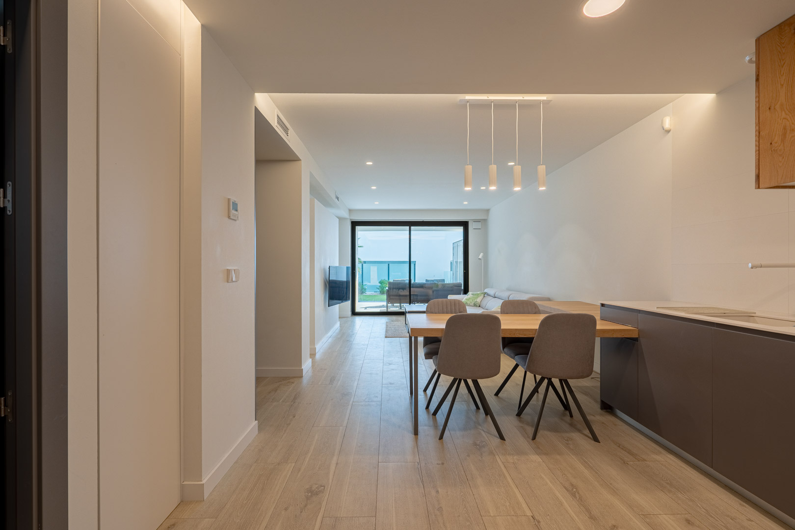 Open-plan living and dining area featuring wood-effect flooring, recessed LED lighting, and large sliding doors opening to the terrace and garden.