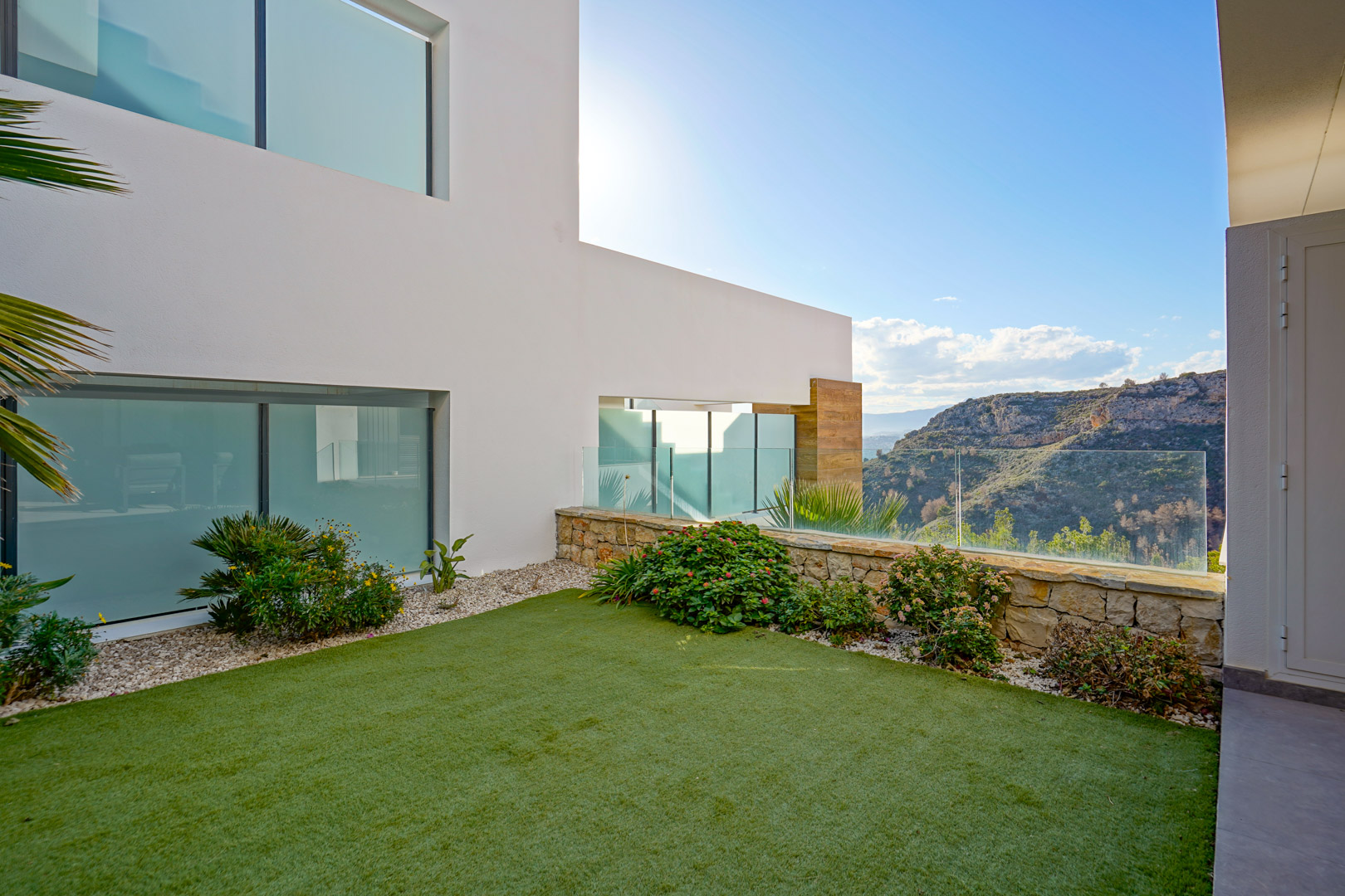 Private garden featuring artificial turf and a natural stone wall with glass railings, overlooking the expansive nature park.
