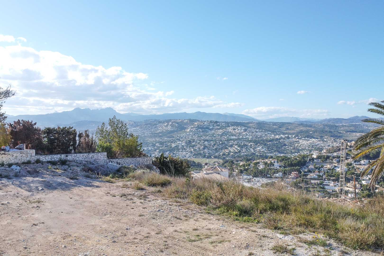 Panoramic view of Moraira from elevated land with stone wall and vegetation.