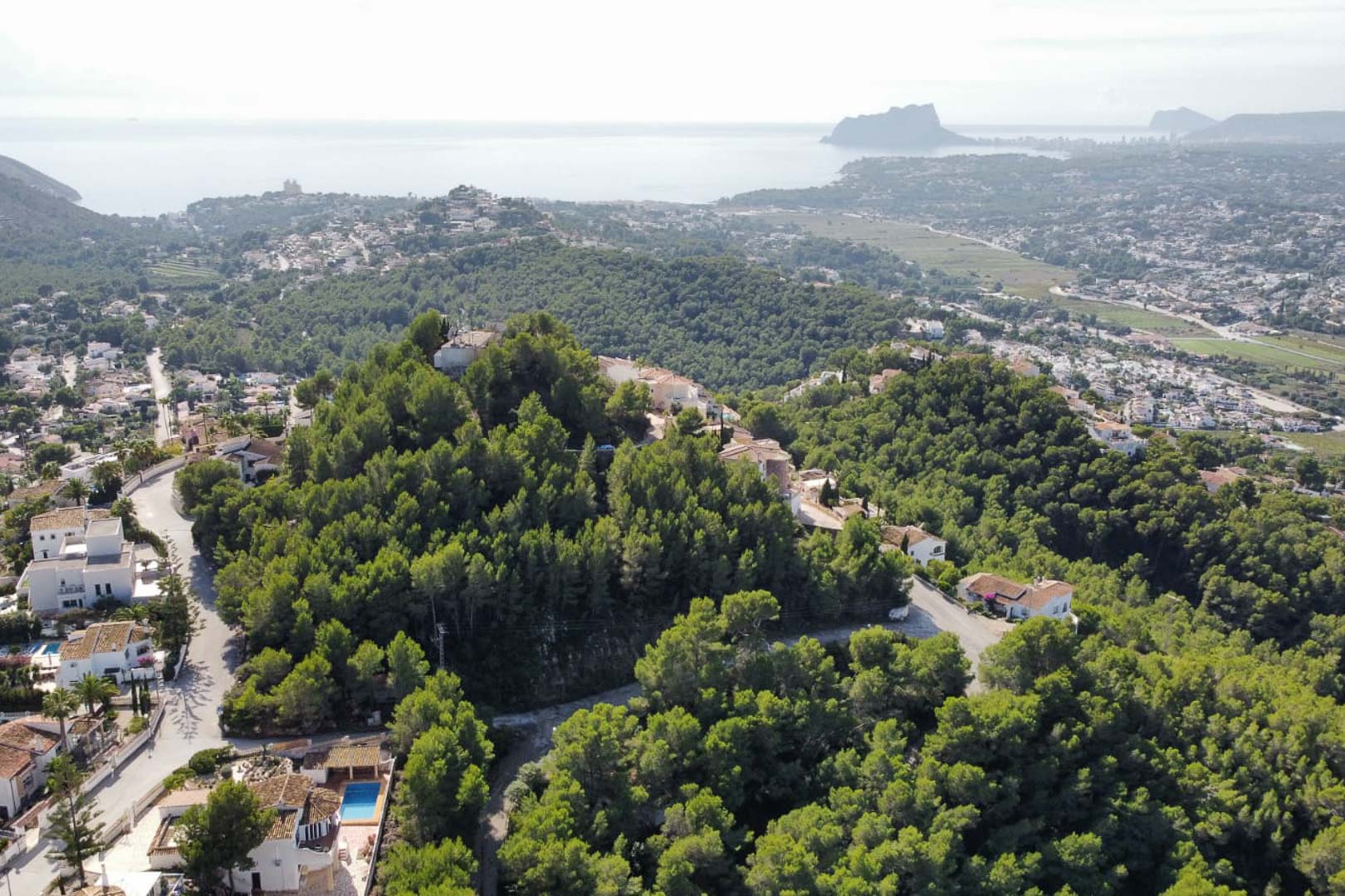 Aerial view of the Paichi residential area in Moraira, featuring dense pine forests and panoramic views of the Mediterranean Sea and the Peñón de Ifach.