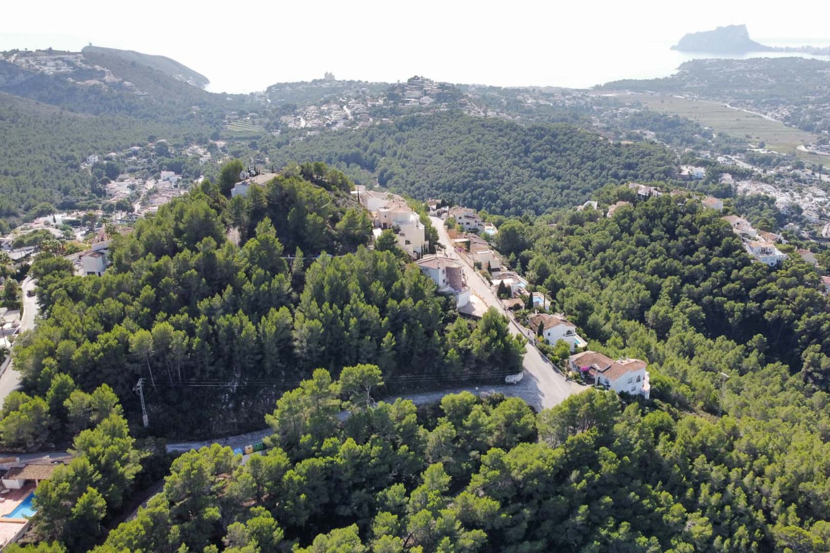Aerial view of the Paichi residential area in Moraira, featuring elevated plots surrounded by pine forests with distant sea views and the Peñón de Ifach.