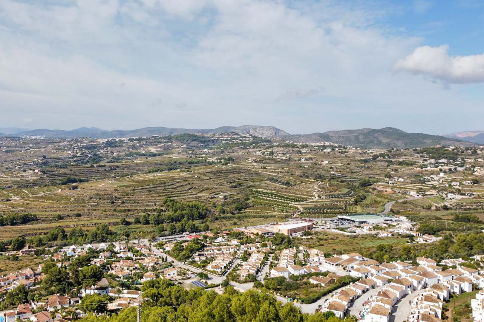 Panoramic aerial view from the Paichi area, showcasing white-walled residential clusters and terraced hillsides leading toward the distant mountain range.