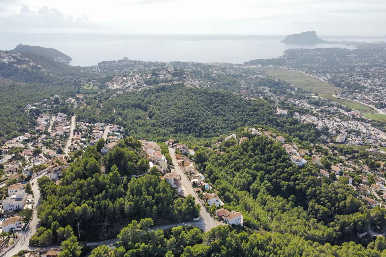 Panoramic aerial view of the Paichi residential area, featuring lush pine forests, detached villas, and the Peñón de Ifach silhouette against the Mediterranean horizon.