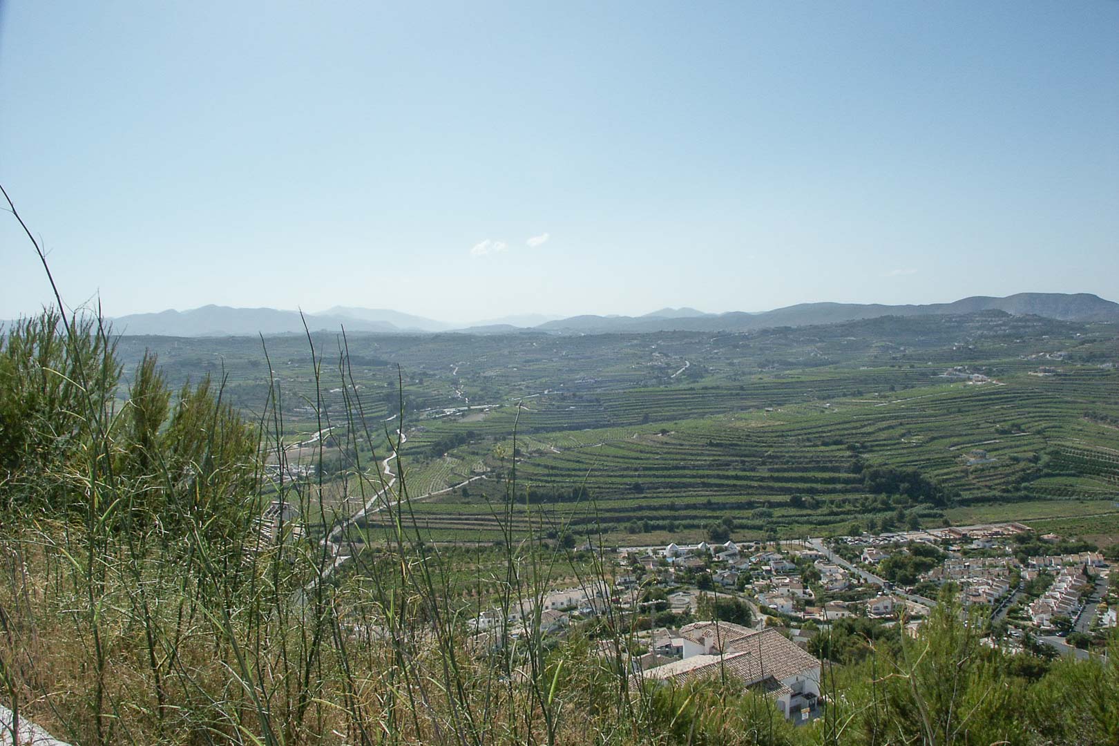 Panoramic view from the elevated plot in Paichi, overlooking terraced agricultural lands and distant mountain ranges under a clear sky.