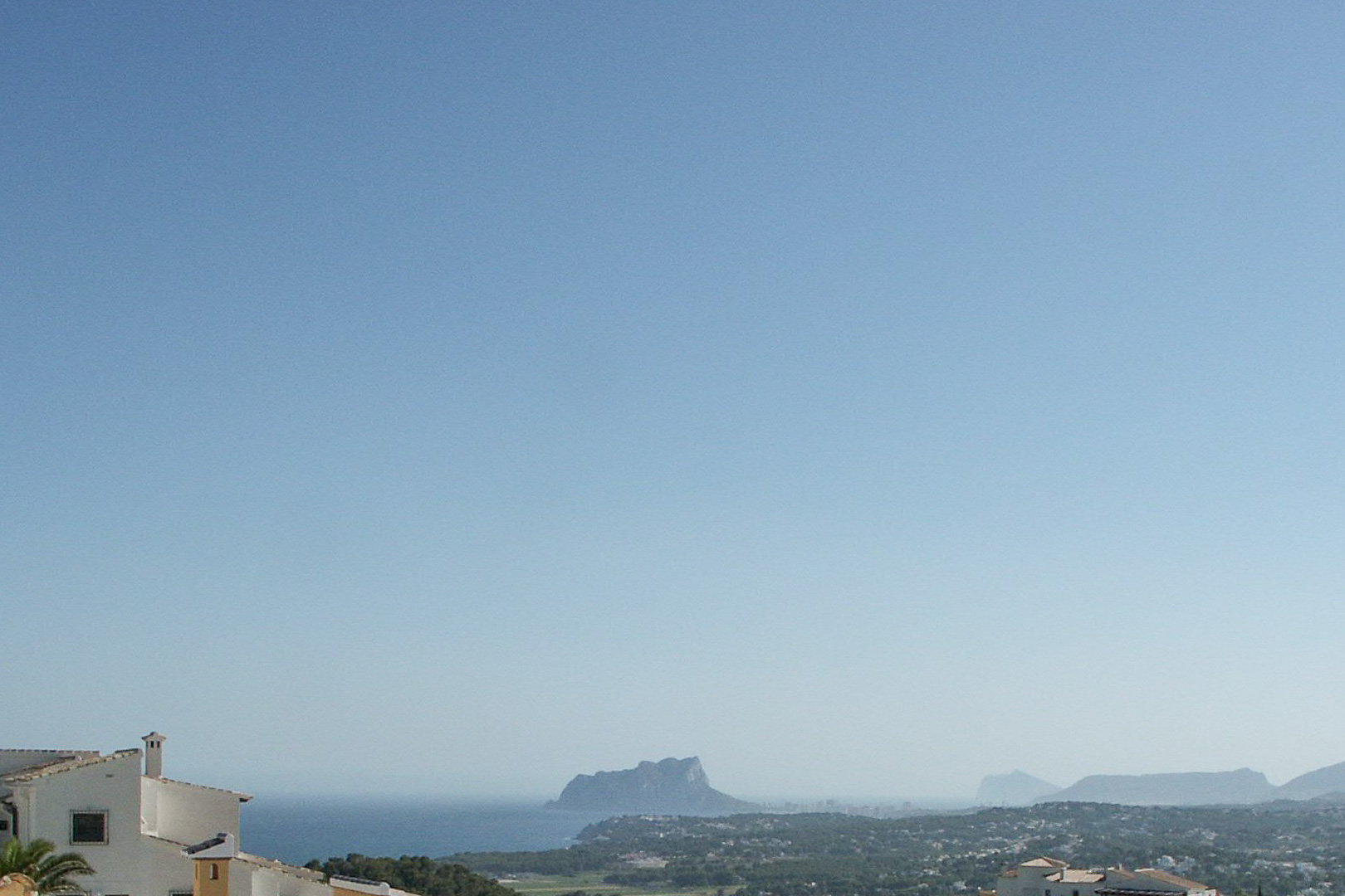 Panoramic view from the elevated plot towards the Calpe coastline, featuring the silhouette of the Peñón de Ifach and the Mediterranean Sea.
