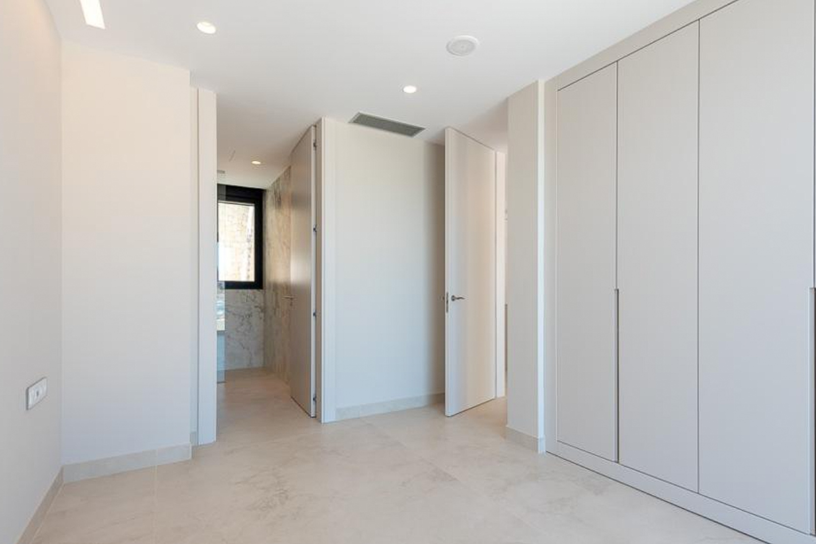 Bedroom featuring floor-to-ceiling built-in wardrobes, recessed ceiling lighting, and a view into an en-suite bathroom with marble wall tiling.